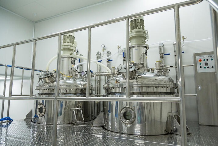 Industrial stainless steel pharmaceutical mixing reactors with top-mounted agitators and a metal safety railing in a clean production facility.